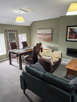 A modern living room with a dining area, a sofa, a coffee table, and a fireplace. - Duplex Apartment in the Heart of Glenarm Village (Ballymena)
