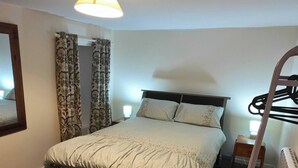 Et soveværelse med seng, natbord, lampe, radiator og et spejl.