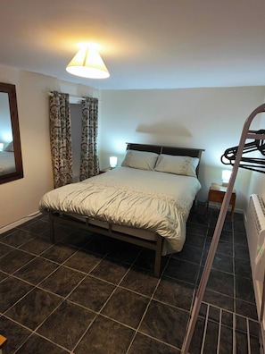 A bedroom with a bed, a nightstand, a lamp, a radiator, and a mirror. - Duplex Apartment in the Heart of Glenarm Village (Ballymena)