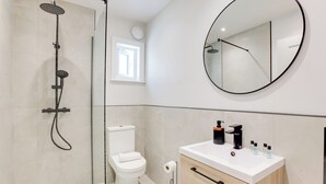 Uma casa de banho moderna com chuveiro, sanita, lavatório e espelho.
