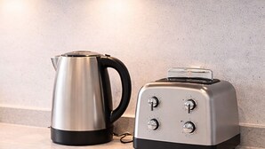 Uma bancada de cozinha com uma chaleira de aço inoxidável e uma torradeira prateada.