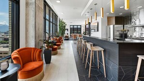 Een moderne hotel lobby met een lange bar, oranje zitplaatsen, grote ramen en uitzicht op de stad.