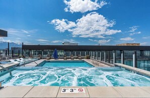 Piscina en la azotea con vistas a montañas, sillas de descanso y un área con paredes de vidrio.