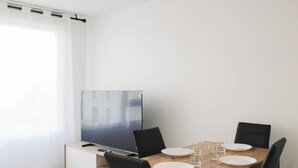 Zona de menjador amb taula ben parada per a quatre persones, televisió de pantalla plana i finestra amb cortines.