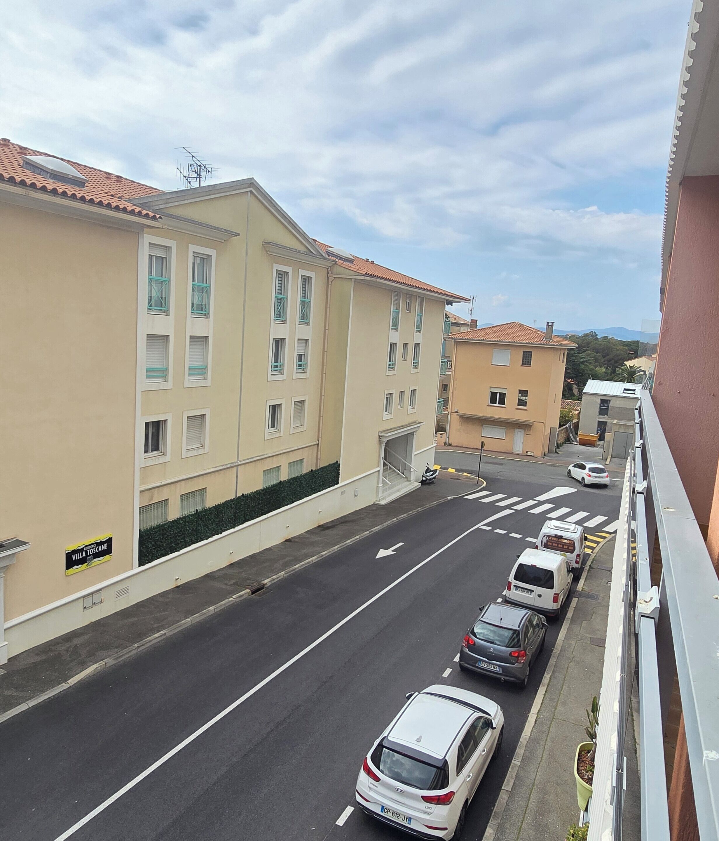 A street view with parked cars, a building with a sign 'Villa Toscana,' and a clear sky.