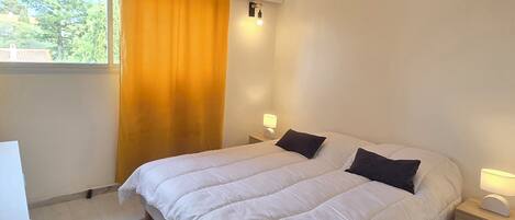 A bedroom with a bed, two bedside tables, a window with curtains, and a wall-mounted light fixture.