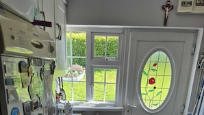 Une buanderie équipée d’un lave-linge, d’un étendoir, d’une fenêtre donnant sur un jardin et d’une porte ornée d’un vitrail.