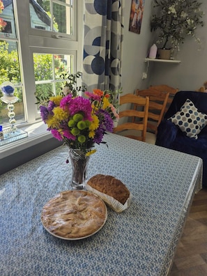 Un coin repas avec une table, des chaises, un vase de fleurs et une miche de pain.