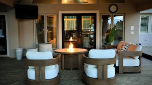 A patio with a round table and two chairs, a fire feature, and a clock on the wall.