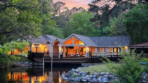A lakeside lodge with a covered outdoor seating area, a dock, and a reflection in the water.