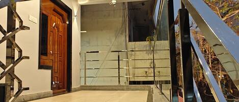 A modern building entrance with a wooden door, a staircase with metal railings, and a concrete floor.