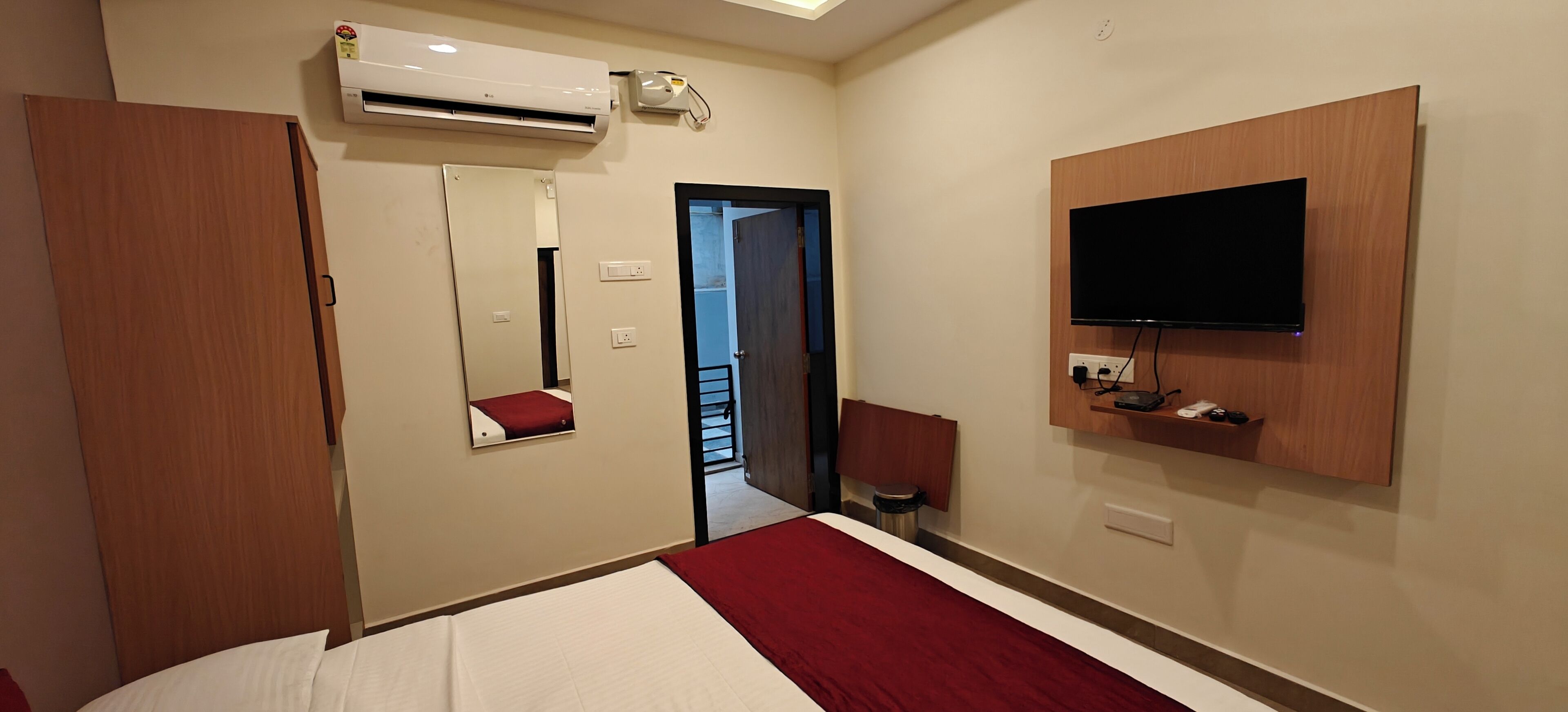 A hotel room with a bed, a TV mounted on the wall, an air conditioning unit, a mirror, and a door leading to a balcony.