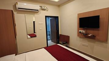 A hotel room with a bed, a TV mounted on the wall, an air conditioning unit, a mirror, and a door leading to a balcony.