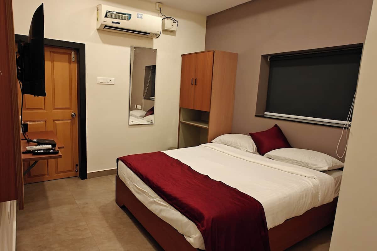 A bedroom with a bed, a wardrobe, a mirror, an air conditioning unit, and a window.