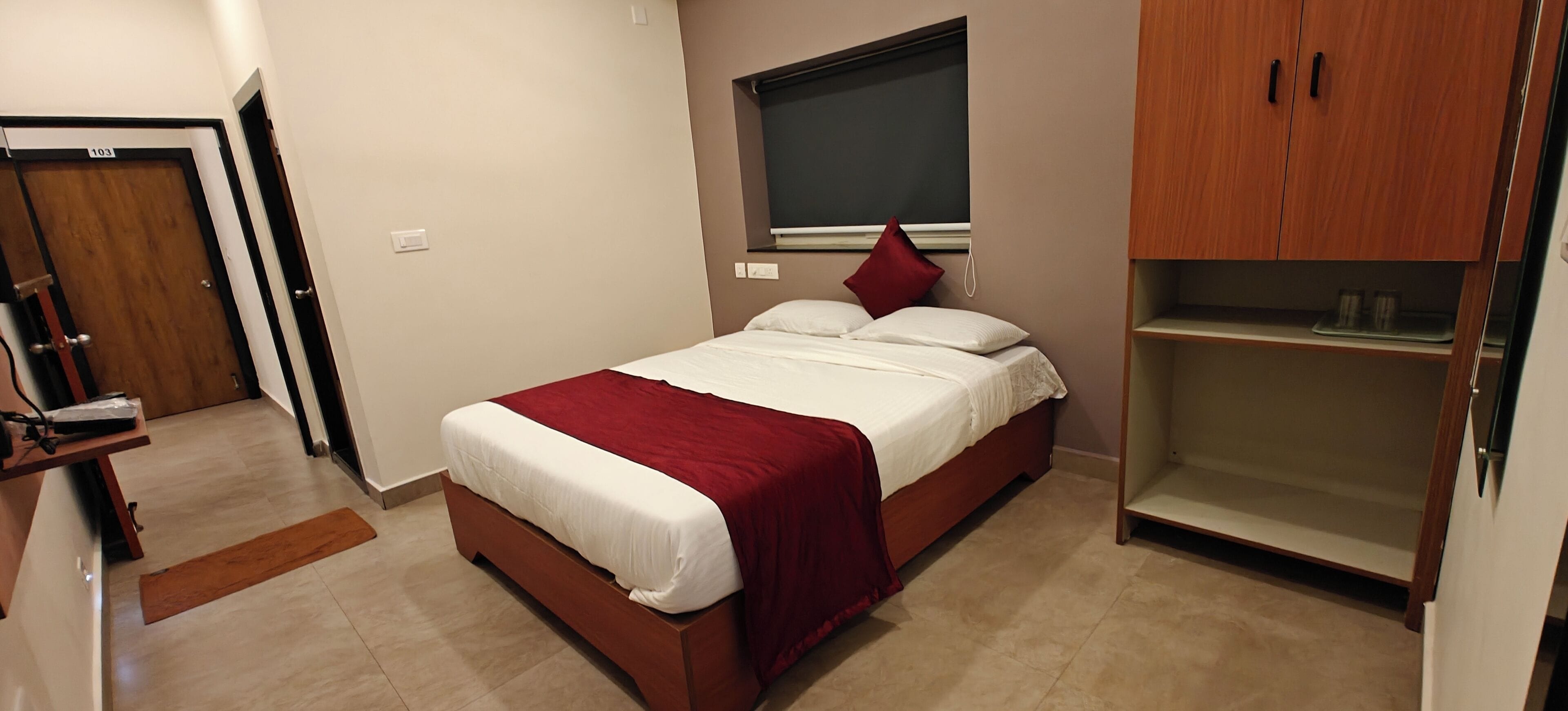 Un dormitorio con una cama, un armario de madera, una ventana con persiana y una puerta con número.