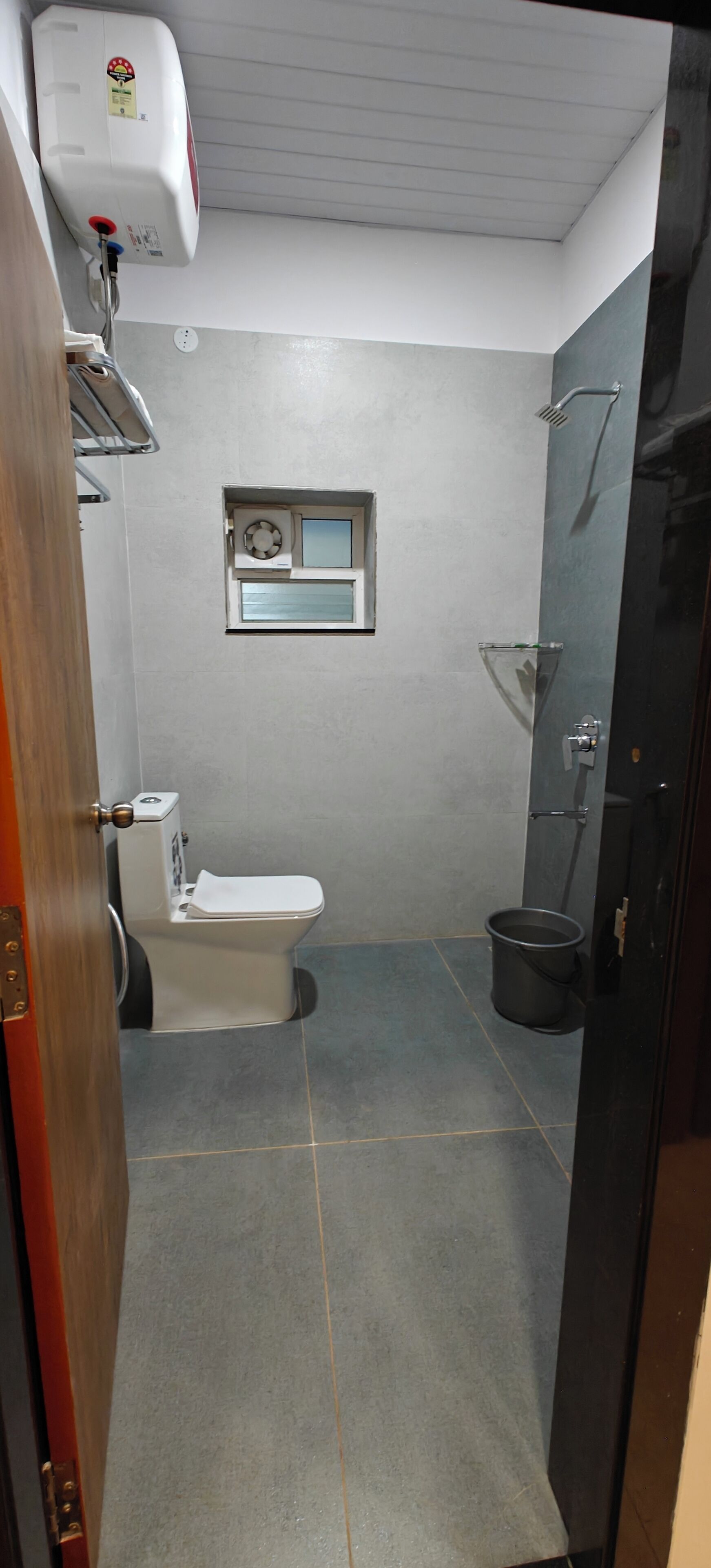 Une salle de bain équipée de toilettes, d’une petite fenêtre, d’une douche et d’un chauffe-eau.