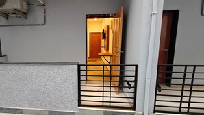 A gated entrance to a building with a tiled floor, a wooden door, and a wall-mounted air conditioning unit. - AKSHAYA COMFORTS (Visakhapatnam)