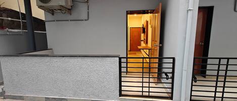 A gated entrance to a building with a tiled floor, a wooden door, and a wall-mounted air conditioning unit.