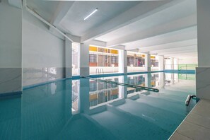 Une piscine intérieure à l’eau claire, avec des murs carrelés et une rambarde visible.