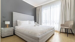 A modern bedroom with a large bed, a bedside table, a chair, and a window with curtains. - Annbell Haven 1br, With Pool, Near Junct (Nairobi)