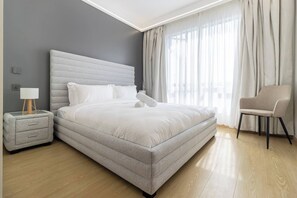 Une chambre à coucher moderne avec un grand lit, une table de chevet, une chaise et une fenêtre avec des rideaux.