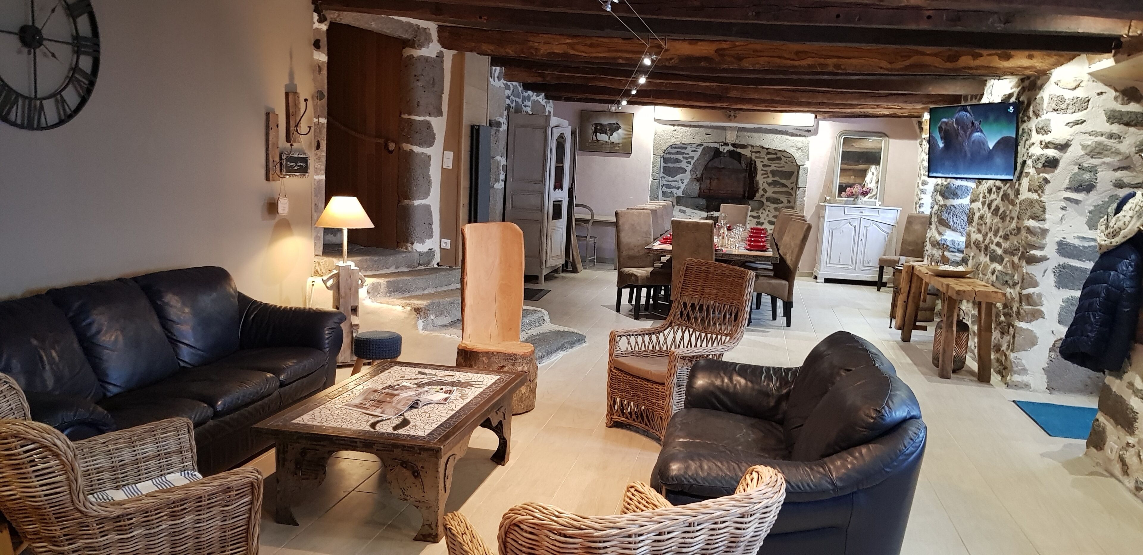 Un interior rústico con chimenea de piedra, sofás de cuero, sillas de mimbre y un comedor con mesa y sillas de madera.