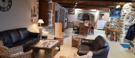 Un interior rústico con chimenea de piedra, sofás de cuero, sillas de mimbre y un comedor con mesa y sillas de madera.