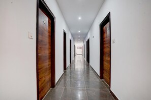 A long, narrow hallway with wooden doors on both sides, a tiled floor, and recessed ceiling lights.