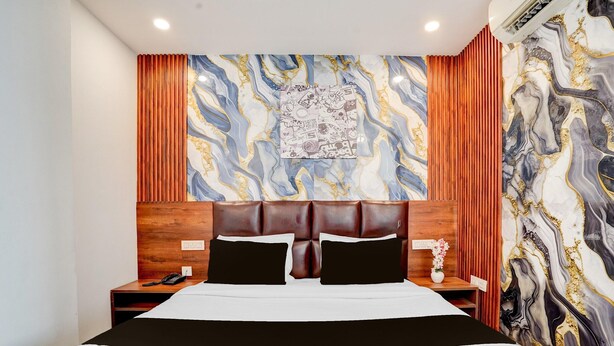 A hotel room with a large bed, wooden headboard, and a marble-patterned wall. - Deluxe Hotel Kc Royal (Dera Bassi)