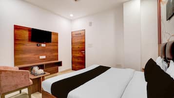 A hotel room with a bed, a TV mounted on a wooden panel, a wooden door, and a small table with a kettle.