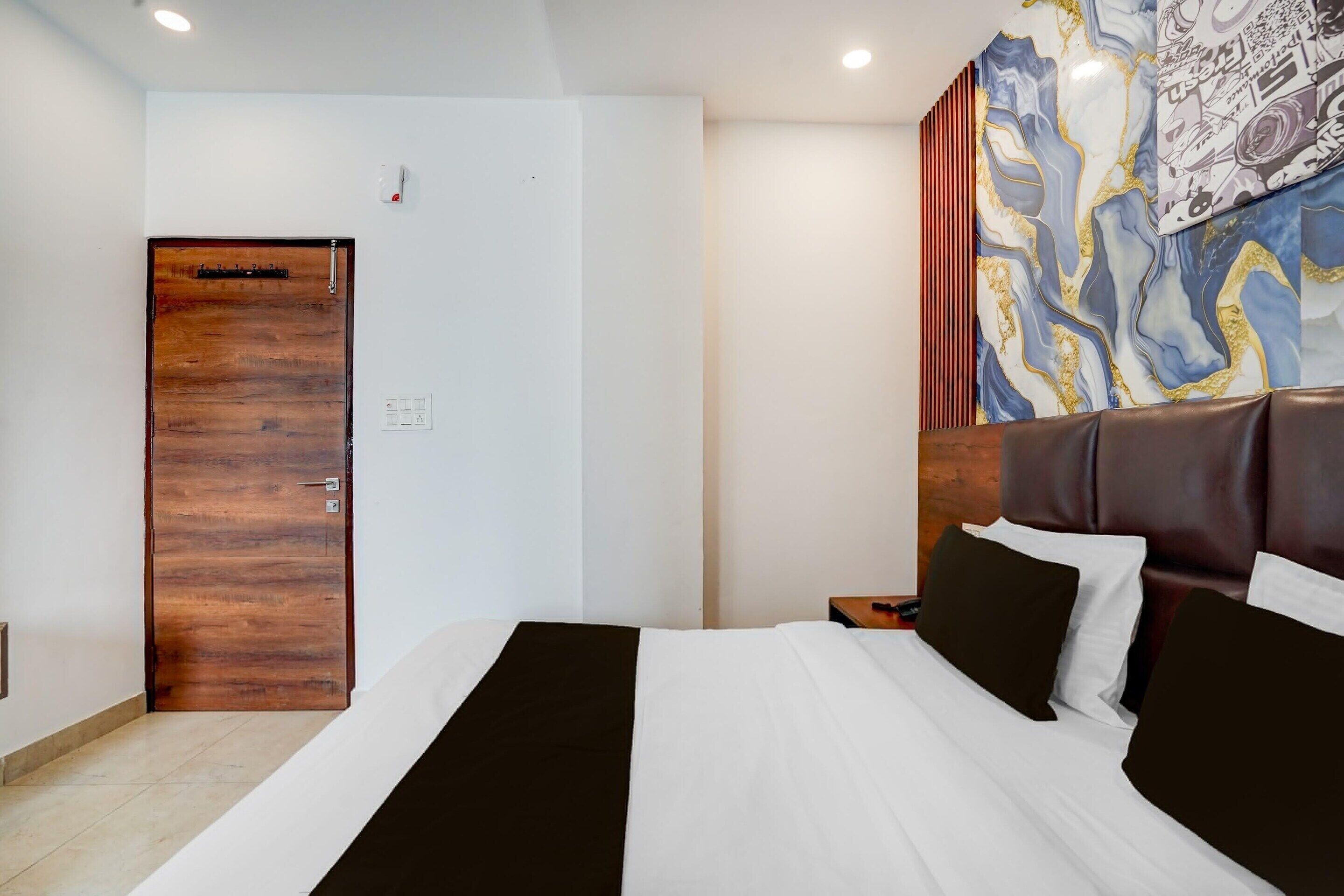 Ein Hotelzimmer mit Holztür, einem Bett mit schwarz-weißer Bettwäsche, einem Nachttisch und einer Wand mit einem farbenfrohen abstrakten Gemälde.