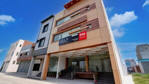 A modern hotel with a flat facade, multiple windows, and a sign advertising a booking app. - Deluxe Hotel Kc Royal (Dera Bassi)