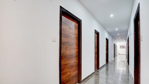 A long, narrow hallway with wooden doors and a tiled floor. - Deluxe Hotel Kc Royal (Dera Bassi)