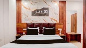 A hotel room with a bed, wooden headboard, a nightstand, a phone, a mirror, and a wall with a 'Hollywood' sign. - Deluxe Hotel Kc Royal (Dera Bassi)