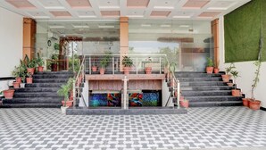 A modern hotel lobby with a central staircase, potted plants, and a patterned floor. - Deluxe Hotel Kc Royal (Dera Bassi)