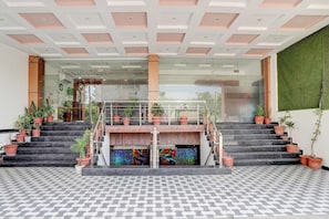 A modern hotel lobby with a central staircase, potted plants, and a patterned floor.