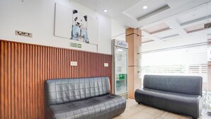 A reception area with a wooden panel wall, a black leather sofa, a refrigerator labeled 'Celfrost,' and a painting of pandas. - Deluxe Hotel Kc Royal (Dera Bassi)