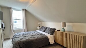 Et soveværelse med seng, sengebord, lampe og radiator.
