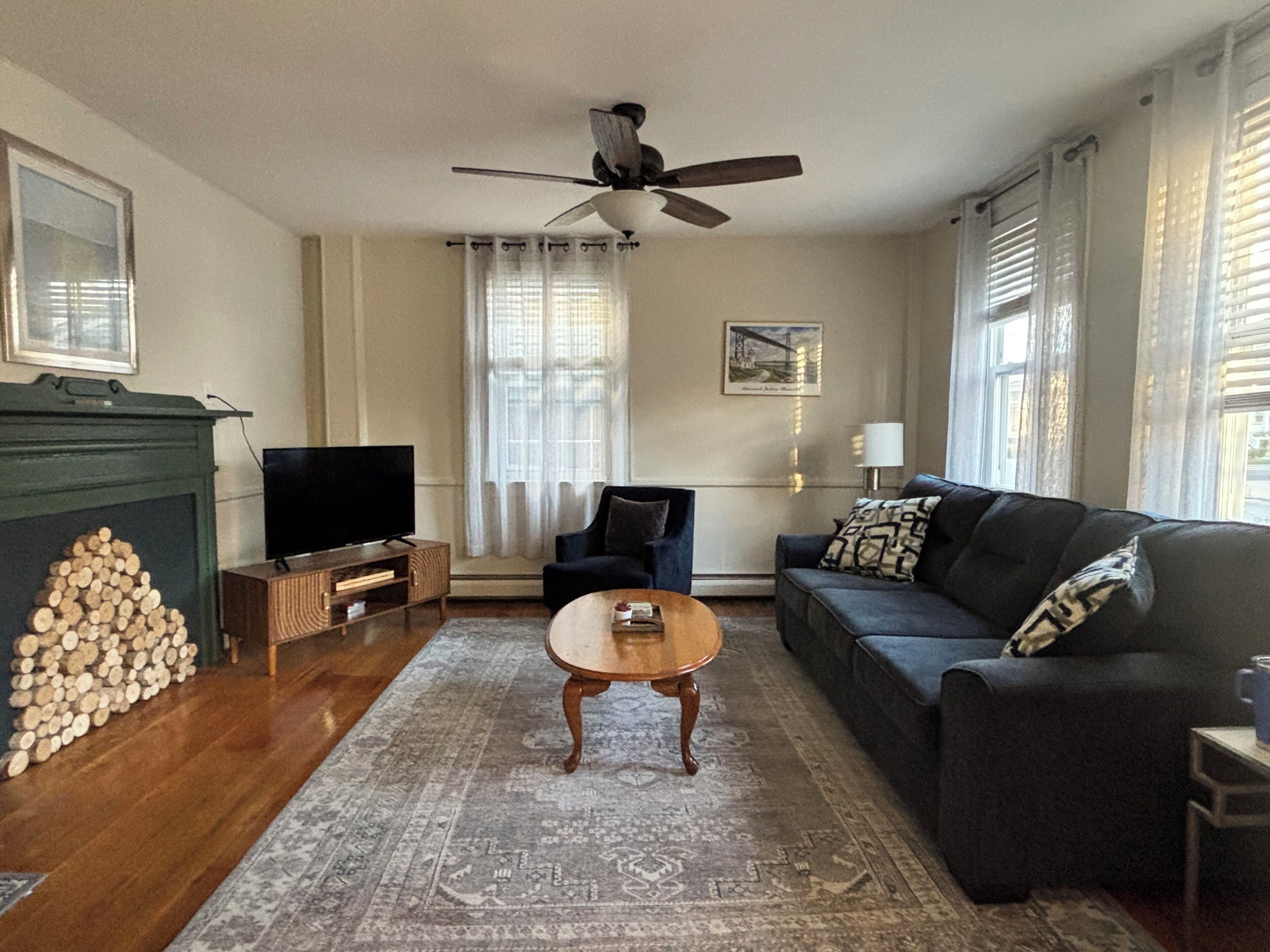Una sala de estar con chimenea, televisor, sofá, mesa de centro y ventilador de techo.