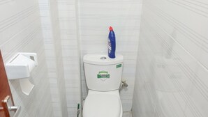 A small, narrow bathroom with white tiled walls and floor, a white toilet, a hand dryer, and a blue bottle on the toilet tank. - Serene 1-bedroom apartment in Nairobi perfect for your stay (Nairobi)