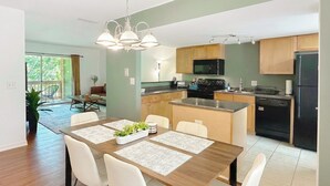 Una cocina moderna con armarios de madera, un refrigerador negro y una zona de comedor con mesa de madera y sillas blancas.