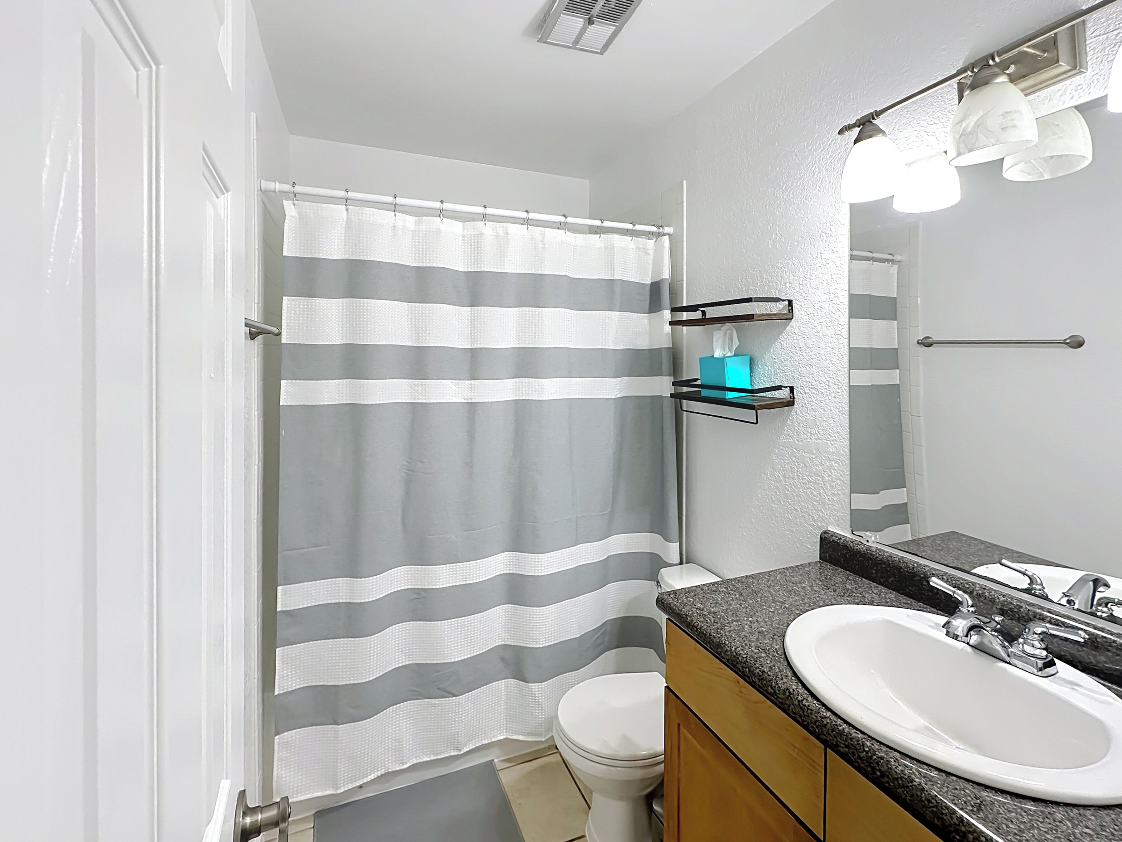 A bathroom with a striped shower curtain, a white sink, and a mirror with lights.