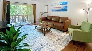 Un salón con sofá, mesa de centro, televisor, sillón verde y un ventanal con vistas al exterior.