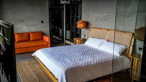 Une chambre moderne avec un grand lit, un canapé, une lampe et une vue à travers une porte vitrée.