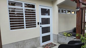 A door with a window, a small porch area with a chair and a potted plant, and a concrete step leading to the door. - King-Bed Room Accessible in Stella, Rincón - right on the beach (Rincón)