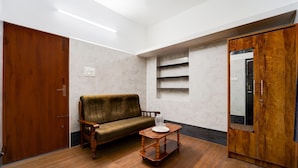 Ein Zimmer mit Holzboden, einer Holztür, einem braunen Sofa, einem kleinen Holztisch und einem Spiegel an der Wand.