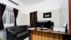 Ein Empfangsschalter mit der Beschriftung 'TOWNHOUSE', eine schwarze Ledersofa, ein Holzstuhl und ein Fenster mit Vorhängen.