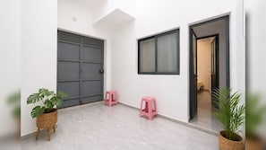 Un couloir propre et moderne, avec une porte grise fermée, une fenêtre et deux tabourets roses.