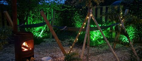 Un cadre extérieur rustique avec un poêle à bois, un hamac et des guirlandes lumineuses.