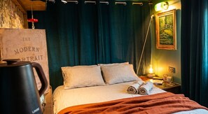 Un lit avec des oreillers, une couverture, une lampe, un tableau et une affiche sur laquelle on peut lire : « Le portrait moderne ».